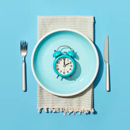 Alarm clock placed on a blue plate with fork and knife, symbolizing intermittent fasting and the science behind time-restricted eating for metabolic health and longevity.