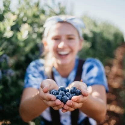 Smiling woman holding freshly picked blueberries in an outstretched hand, symbolizing natural sources of resveratrol.