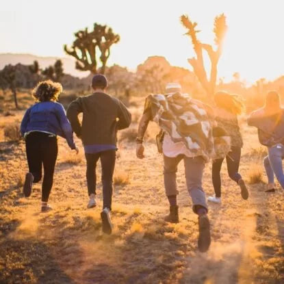 Group of young adults running together through a sunlit desert landscape, symbolizing vitality, energy, and the active lifestyle often associated with NMN supplementation and its potential anti-aging effects.