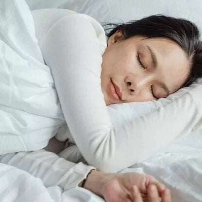 Peaceful woman sleeping on a white bed, representing effective techniques and a calm environment for learning how to fall asleep naturally and improve sleep quality.