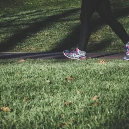 Person walking on a park path in athletic shoes, symbolizing the importance of maintaining energy levels through aging with regular physical activity.