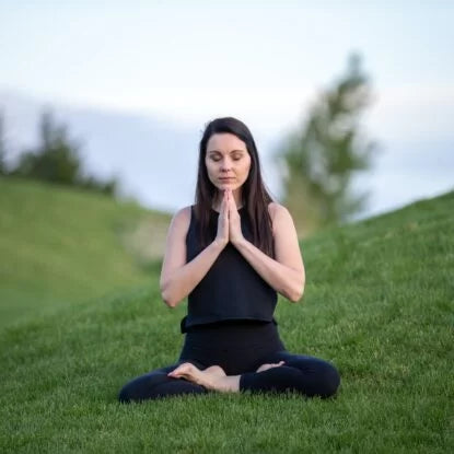 Woman practicing mindfulness and deep breathing outdoors while sitting cross-legged on grass—illustrating calming breathing exercises for stress relief and mental clarity.