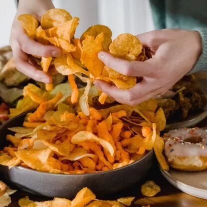Close-up of hands grabbing chips from a bowl filled with processed snacks—highlighting foods linked to premature aging.