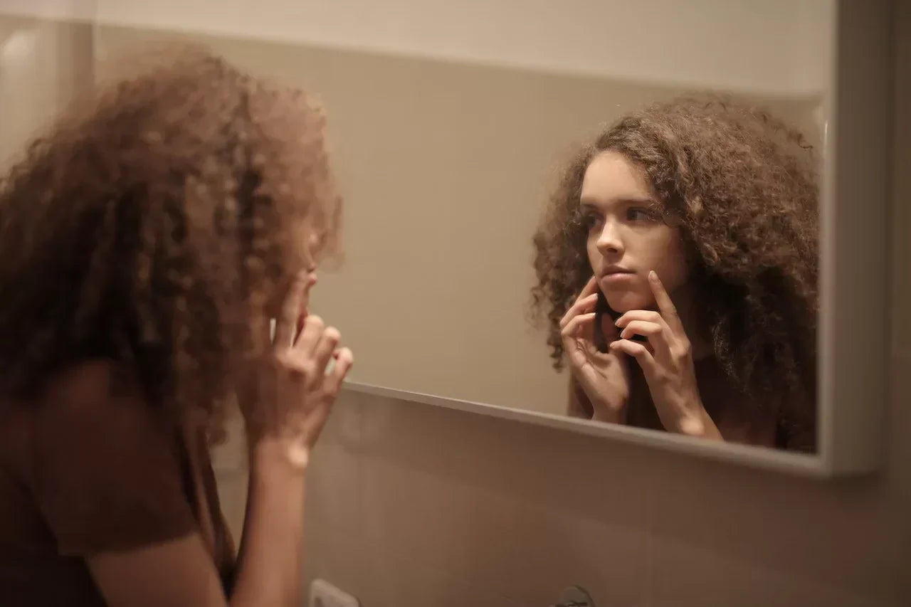 Young woman examining her skin in the mirror, symbolizing the connection between NAD+ levels and skin health, including aging, repair, and cellular rejuvenation.