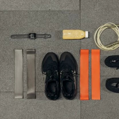 Flat lay of biohacking essentials including resistance bands, smart watch, sneakers, jump rope, and a health drink—representing tools used to optimize health and slow aging through biohacking practices.