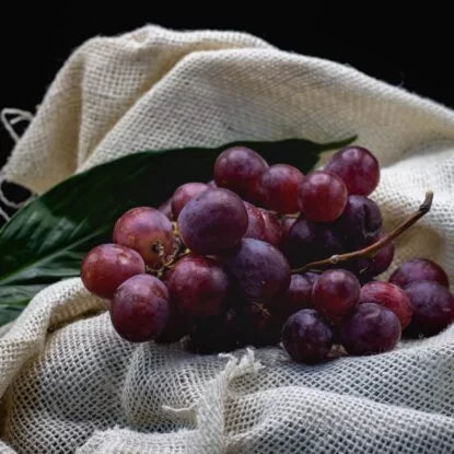 A bunch of fresh red grapes resting on white fabric, representing antioxidant-rich foods that may support a healthy lifespan and the possibility of living to 100.