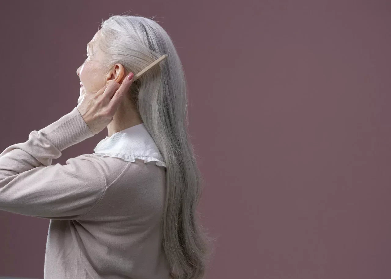 Side view of an older woman gently combing her long silver hair—illustrating discussions on vitamins and supplements that may help slow or reverse premature graying.