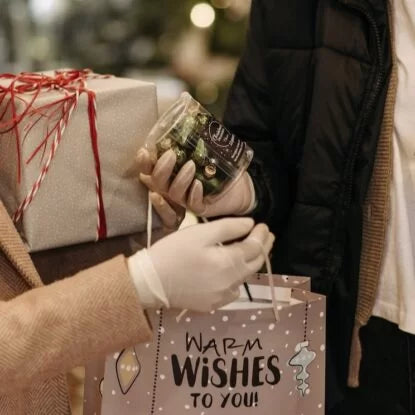 Two people exchanging a holiday gift bag labeled “Warm Wishes to You!”—a thoughtful and festive gesture for healthy gift ideas.