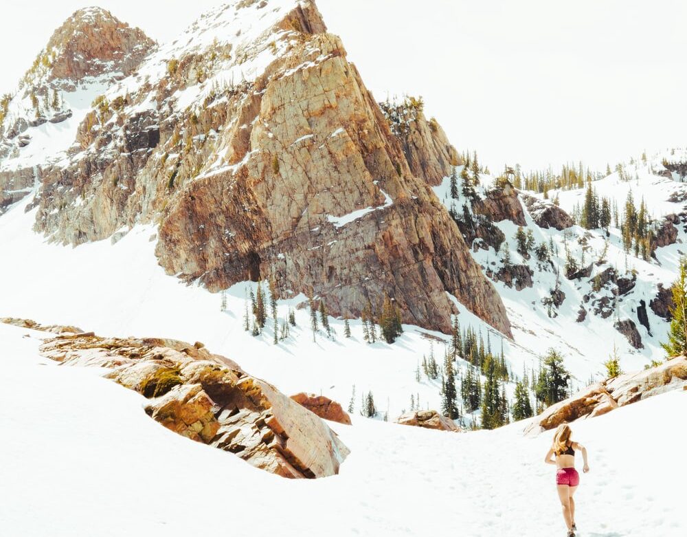 A girl in pink shorts running in the snowy mountains. Healthy lifestyle.