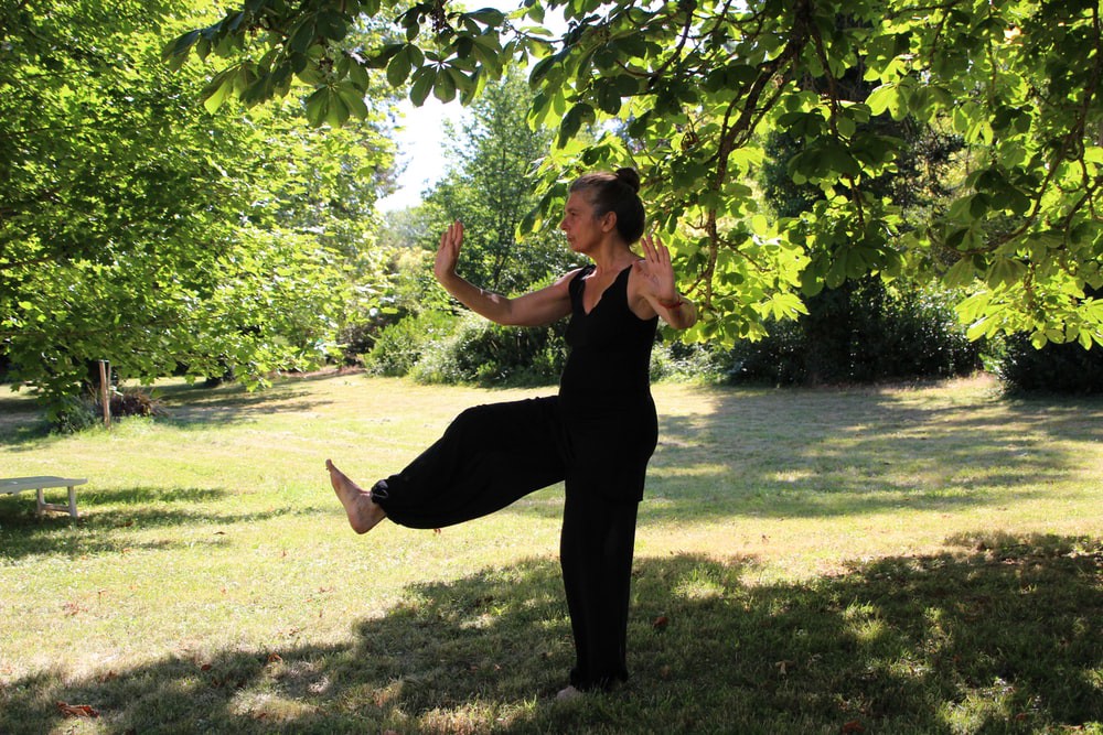 A old woman in black clothes in her garden practicing meditation, Tai-Chi